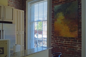 A kitchen with white cabinets, a window with blinds, and a brick wall. - "Caroline" Julia Street Condo with Balcony (New Orleans)