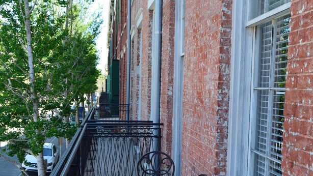 A balcony with metal chairs and tables, brick walls, and a view of the street.