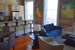 A modern living space with a blue sofa, a dining table with chairs, and a kitchen area with cabinets and appliances.