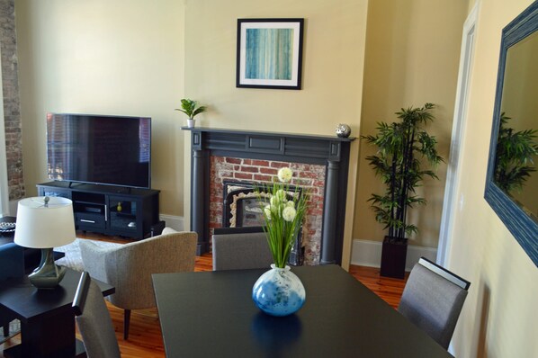 A living room with a fireplace, a flat-screen TV, and a dining area with a table and chairs.