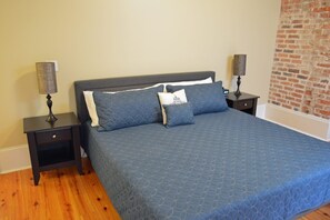 A bedroom with a large bed, two nightstands, a lamp on each, and a brick wall.