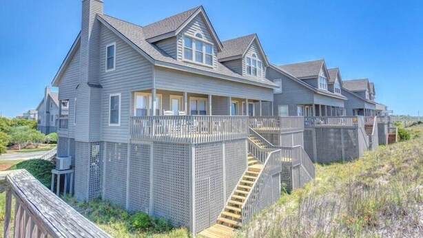 Ein großes, zweistöckiges Strandhaus mit überdachter Veranda und einer Holzterrasse.