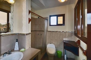 A bathroom with a sink, toilet, shower, and a small window.