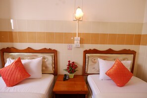 A hotel room with two beds, each with a wooden headboard, white bedding, and a red pillow. There is a nightstand with a remote control and a small potted plant between the beds. - Mitaree Hotel 1 (Mae Sariang)