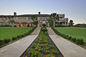 Ein großes, elegantes Gebäude mit symmetrischer Fassade, einem zentralen Eingang und einem gepflegten Garten mit einem Weg zum Eingang.