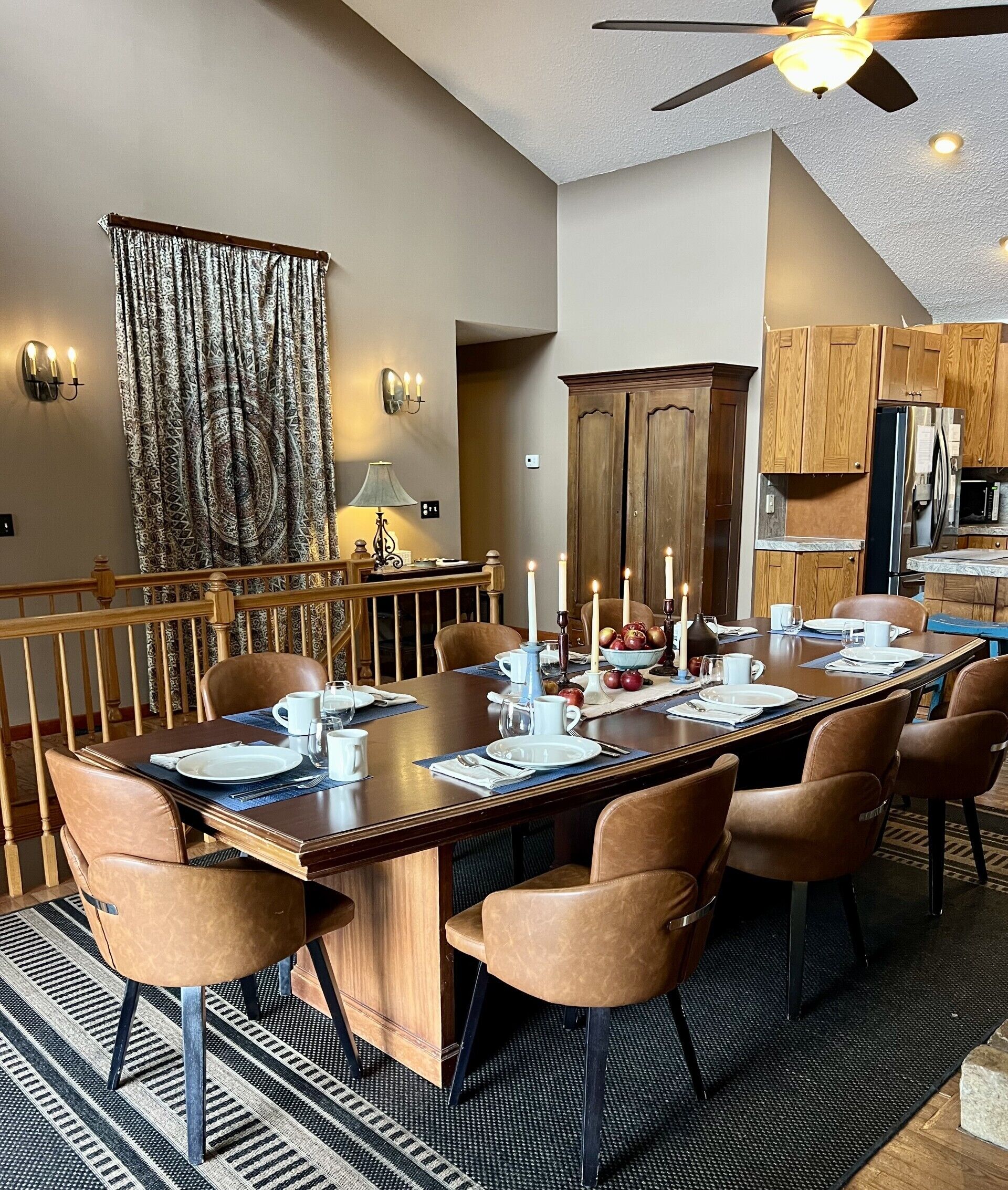 Un comedor con una mesa larga, sillas, velas y una cocina al fondo.