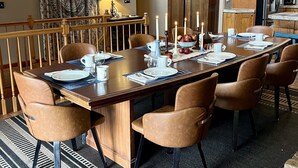 Een eetruimte met een lange tafel, stoelen, kaarsen en een keuken op de achtergrond.