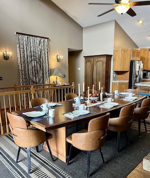 Un espace repas avec une longue table, des chaises, des bougies et une cuisine en arrière-plan.