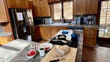 A kitchen with wooden cabinets, a stainless steel refrigerator, a stove, and a window with a view of trees.