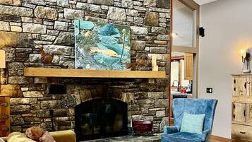 Una sala de estar con chimenea de piedra, ventilador de techo y un sillón azul.