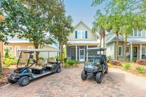 A golf cart parked in front of a house with a brick driveway and a well-maintained lawn.
