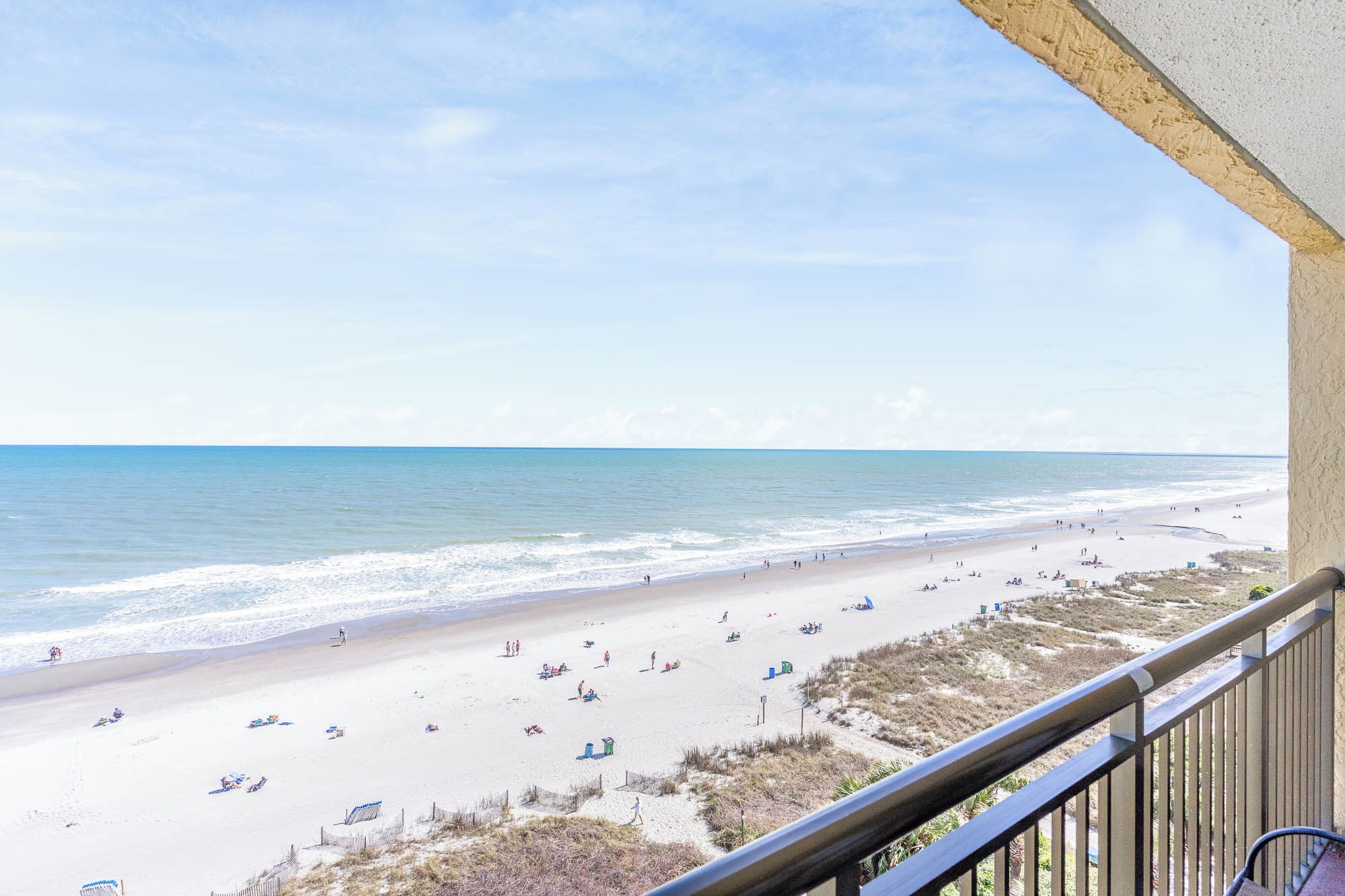 Une vue sur la plage depuis un balcon doté d’une balustrade, avec une plage de sable et l’océan en toile de fond.