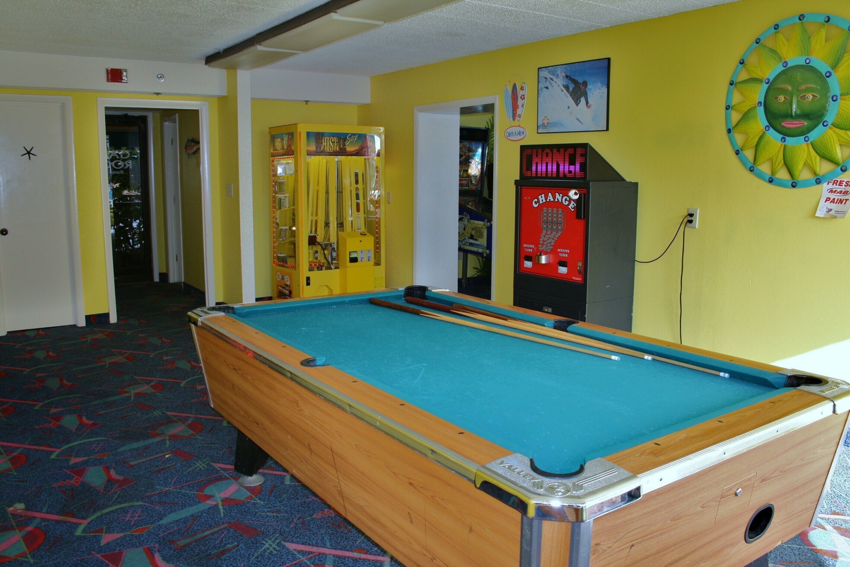 A pool table in a room with yellow walls, a door, and a vending machine.