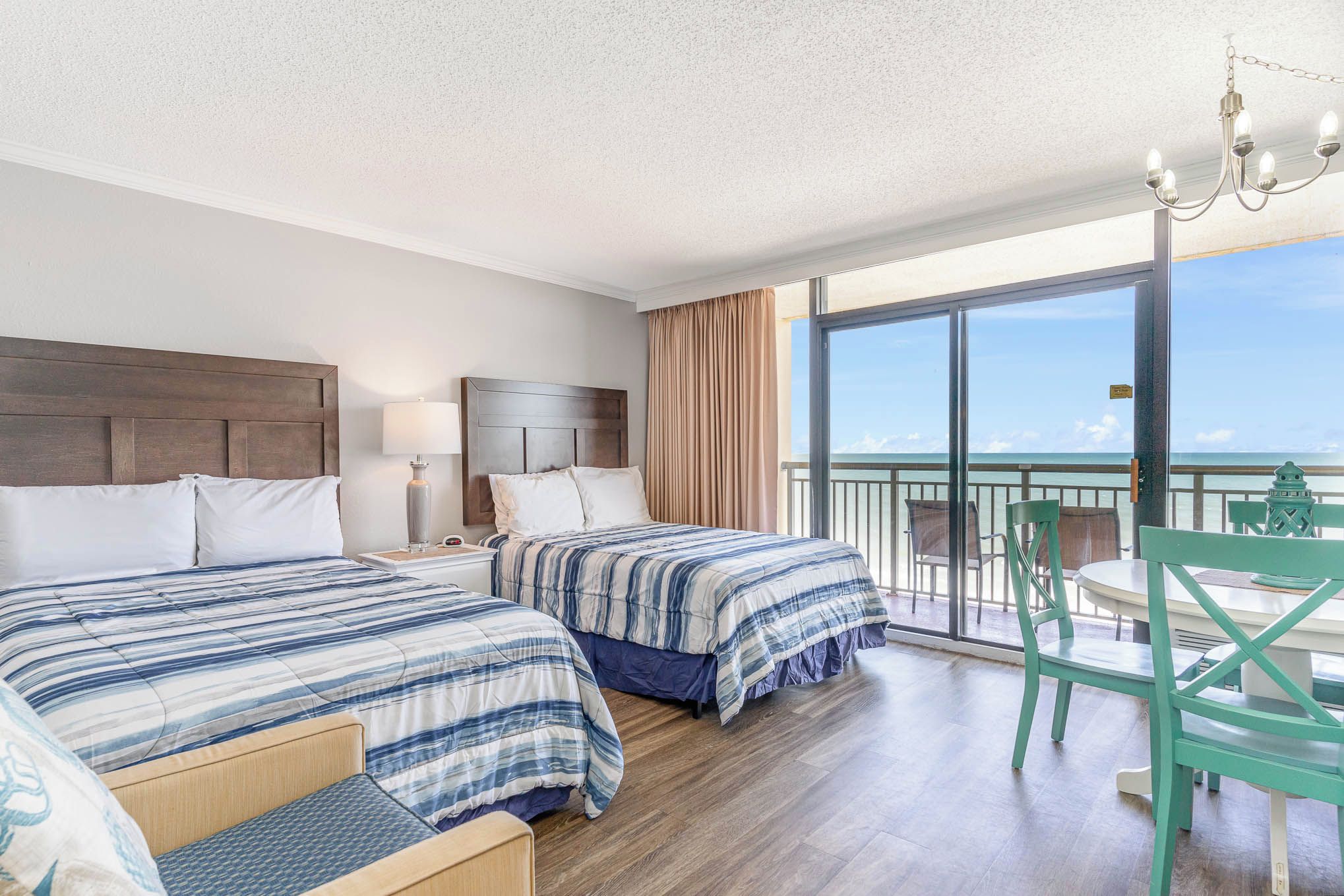 A hotel room with two beds, a balcony with a table and chairs, and a view of the ocean.