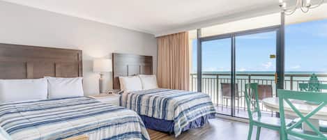 A hotel room with two beds, a balcony with a table and chairs, and a view of the ocean.