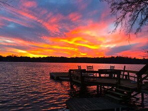 A wooden dock extending into a lake with chairs and tables, surrounded by trees.