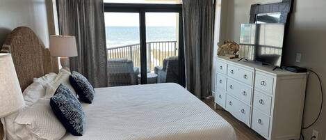A bedroom with a large bed, a dresser, a television, and a view of the ocean.