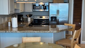 A modern kitchen with granite countertops, stainless steel appliances, and a glass dining table. - Lovely Oceanfront Condo with Gorgeous View with 3 Beds\3 Baths (North Myrtle Beach)