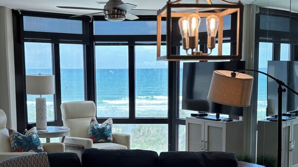 A modern living room with a glass table, a ceiling fan, and a view of the ocean. - Lovely Oceanfront Condo with Gorgeous View with 3 Beds\3 Baths (North Myrtle Beach)