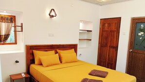 Une pièce comprenant un lit, une table de chevet, une lampe fixée au mur, une porte en bois et une fenêtre avec des rideaux.