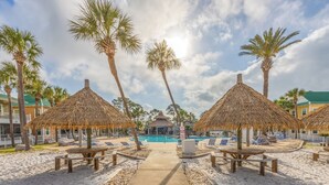 Un resort con sombrillas de techo de paja, piscina y zona de playa arenosa.