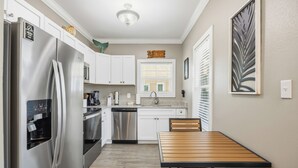 Una cocina compacta con armarios blancos, electrodomésticos de acero inoxidable y una mesa de comedor de madera.