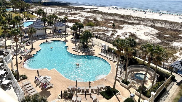 A resort with a large pool, beach access, and palm trees.