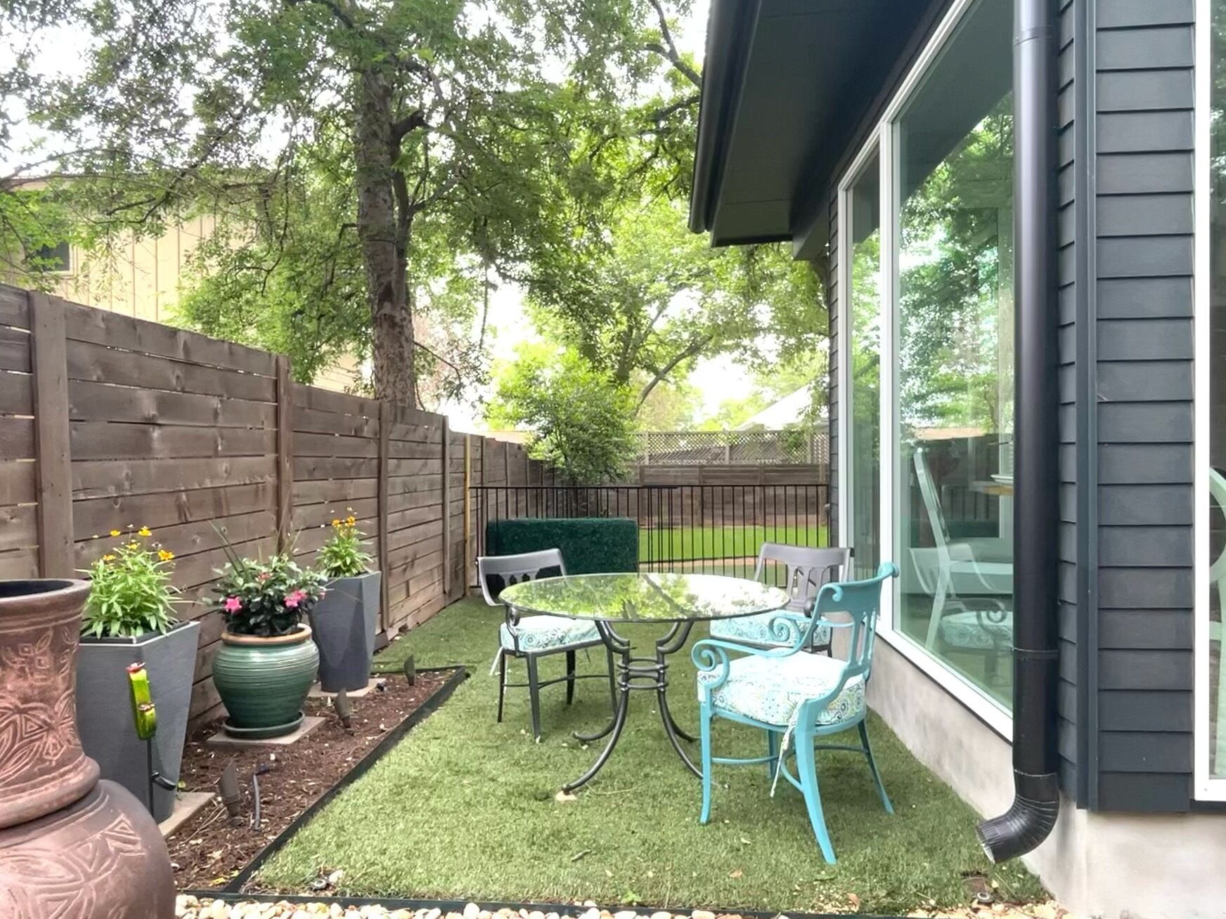Een terras met een tafel en stoelen, omgeven door plantenpotten en een houten hek.