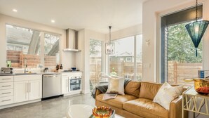 A modern kitchen with white cabinets, a dining area with a brown leather couch, and large windows offering a view of the outdoors. - Bright Contemporary Guest House with Private Patio, Walk to S Congress, Downtown (Austin)