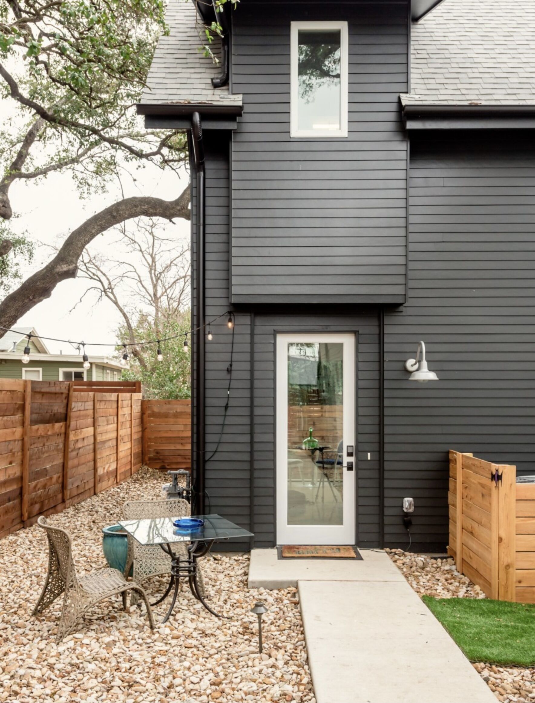 A dark grey house with a small deck, a glass door, and a wooden fence.