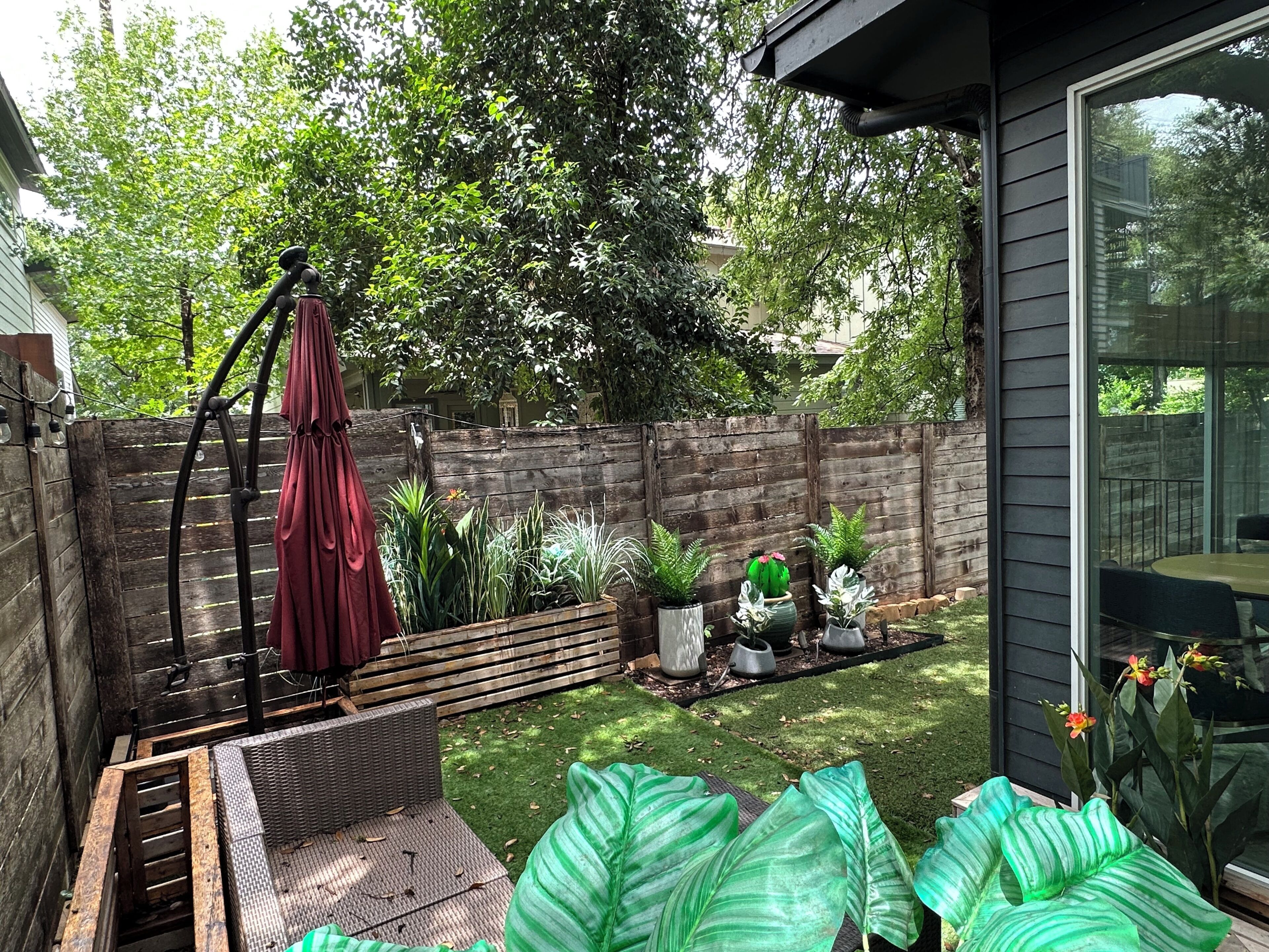 A patio with a wicker sofa, a red umbrella, and potted plants.