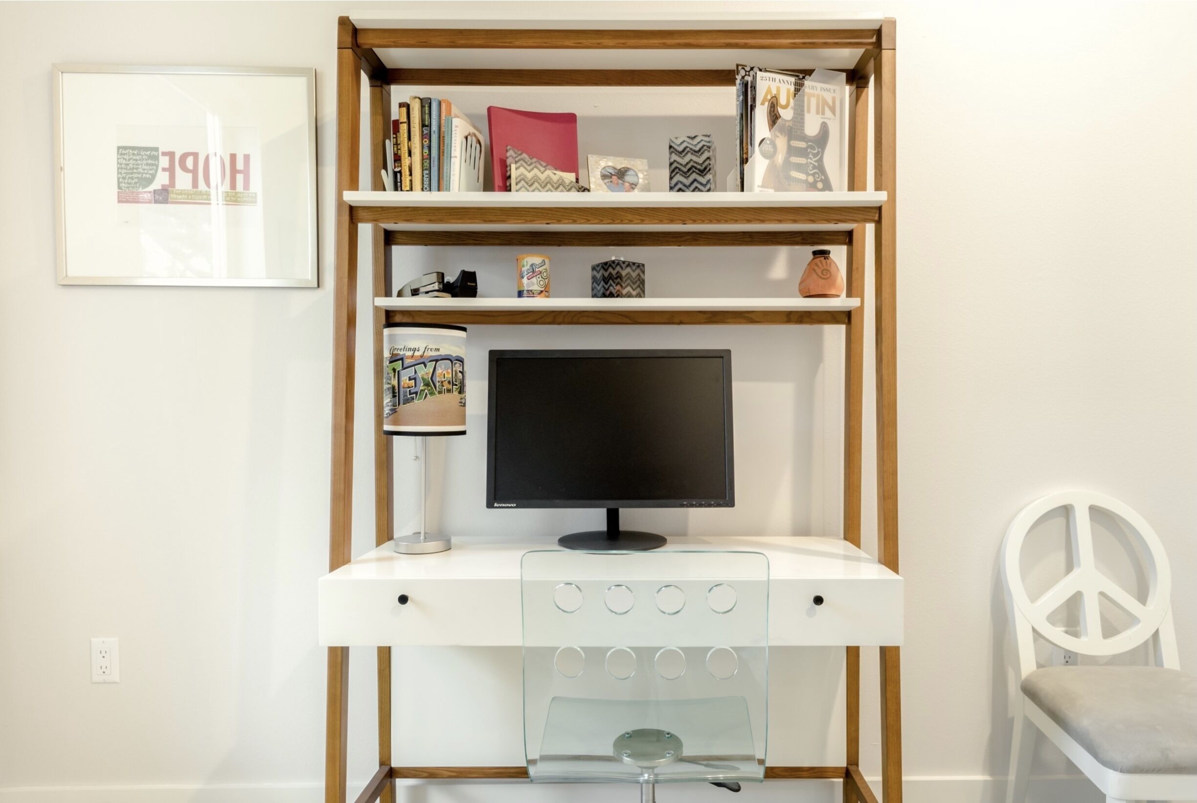 A white desk with a computer monitor, a glass-fronted cabinet, and a peace sign chair.