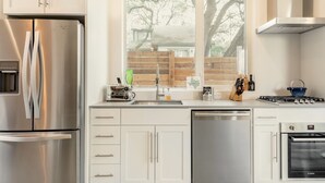 A modern kitchen with stainless steel appliances, white cabinetry, a window with a view of trees, and a dishwasher. - Bright Contemporary Guest House with Private Patio, Walk to S Congress, Downtown (Austin)