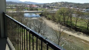 Vista desde un balcón sobre un río, un puente y un pueblo con edificios y montañas a lo lejos.