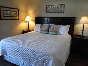 A neatly made bed with a quilted white bedspread, two bedside lamps, a dark wooden headboard, and a framed botanical print on the wall. - 50.00 October-stay gift card! Luxurious Condo, Riverfront w/ Mountain Views! (Sevierville)