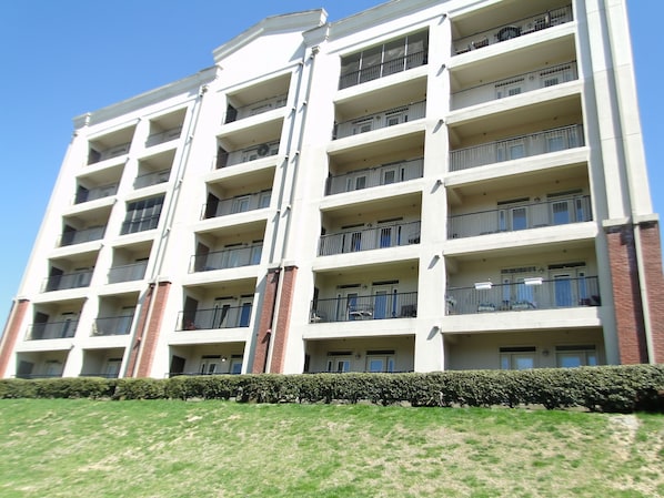 A multi-story residential building with balconies, brick accents, and a well-maintained lawn.