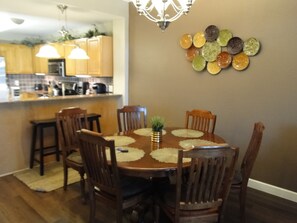 A dining area with a round table surrounded by wooden chairs, a small plant centerpiece, and a wall-mounted plate decoration.