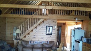 A cozy cabin interior with a wooden staircase, a sofa, a coffee table, and a kitchenette.