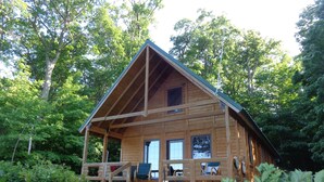 A wooden cabin with a porch, surrounded by trees.