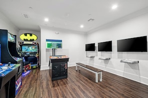 A room with arcade games, a bench, and three mounted TVs.