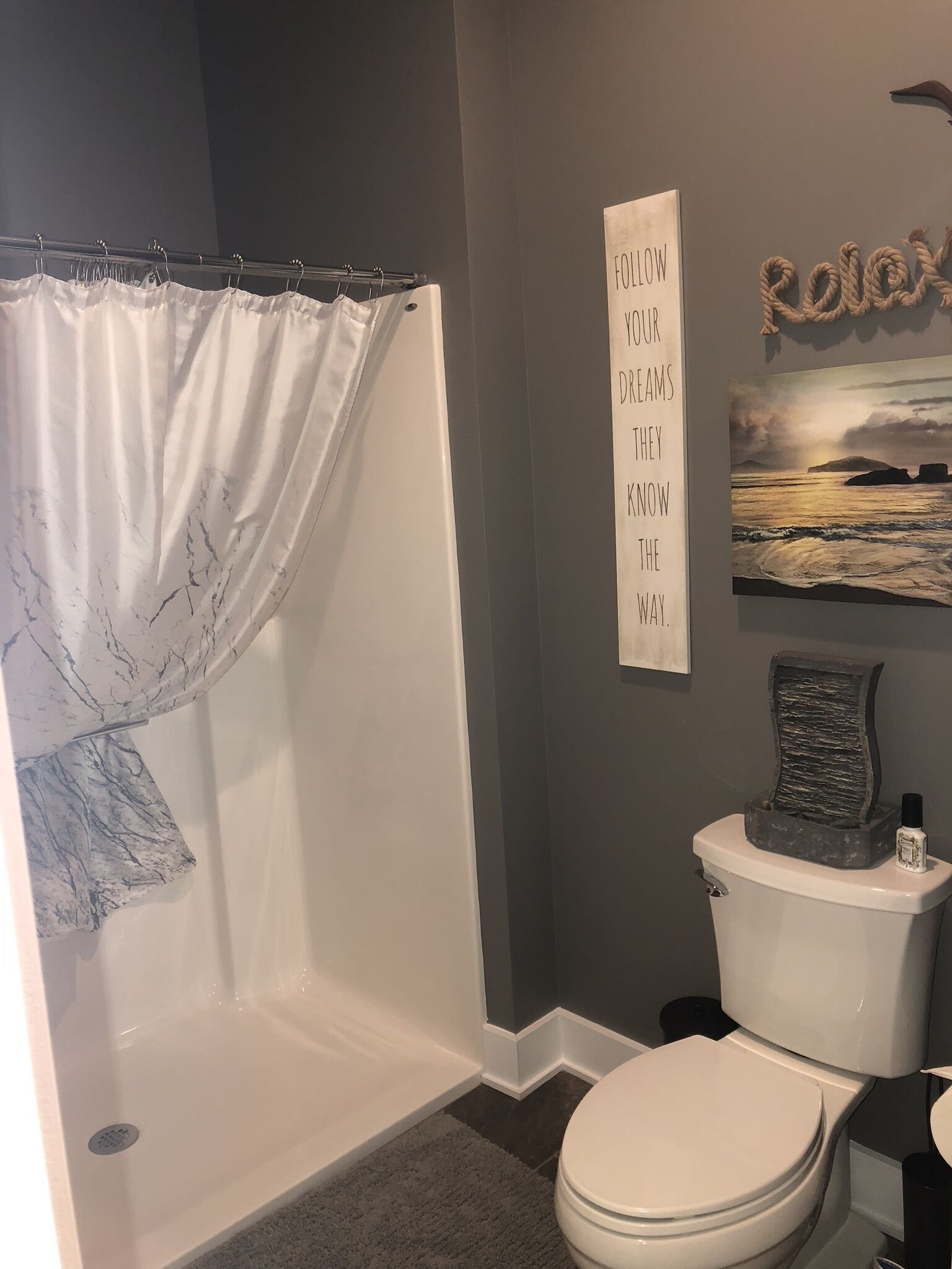 Un baño con cortina de ducha, inodoro y una frase motivacional en la pared.