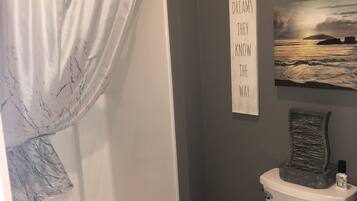 Un baño con cortina de ducha, inodoro y una frase motivacional en la pared.