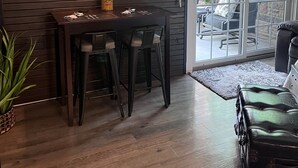Eine moderne Küche mit einer Holzwand, zwei Pendelleuchten, einem Esstisch mit Barhocker und einer Schiebetür aus Glas zum Außenbereich.
