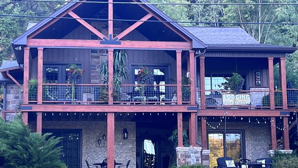 Una cabaña de dos pisos con balcón, mobiliario exterior y un letrero que dice 'Lodging'.