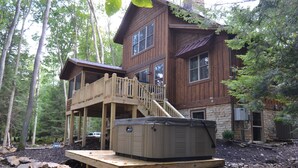 A wooden cabin with a hot tub on a wooden deck, surrounded by trees.