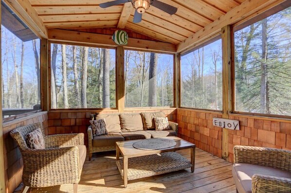 Relax in a peaceful forest setting with a cozy porch featuring a sofa, armchairs, and a large window.
