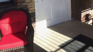 Une porte blanche avec un panneau de verre, un fauteuil rouge rembourré et une petite fenêtre avec des stores.