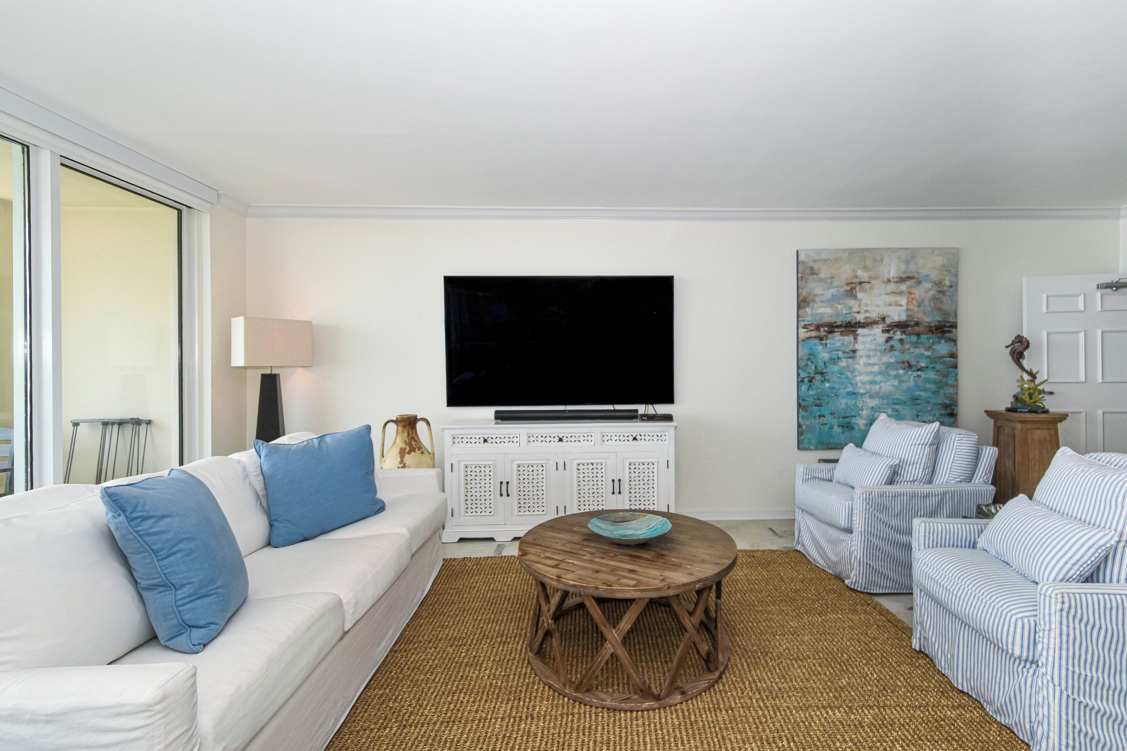 A living room with a white sofa, a striped armchair, a wooden coffee table, a television, and a painting on the wall.