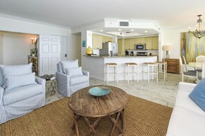Sala de estar com sofá listrado, mesa de centro de madeira e área de cozinha com um banco.