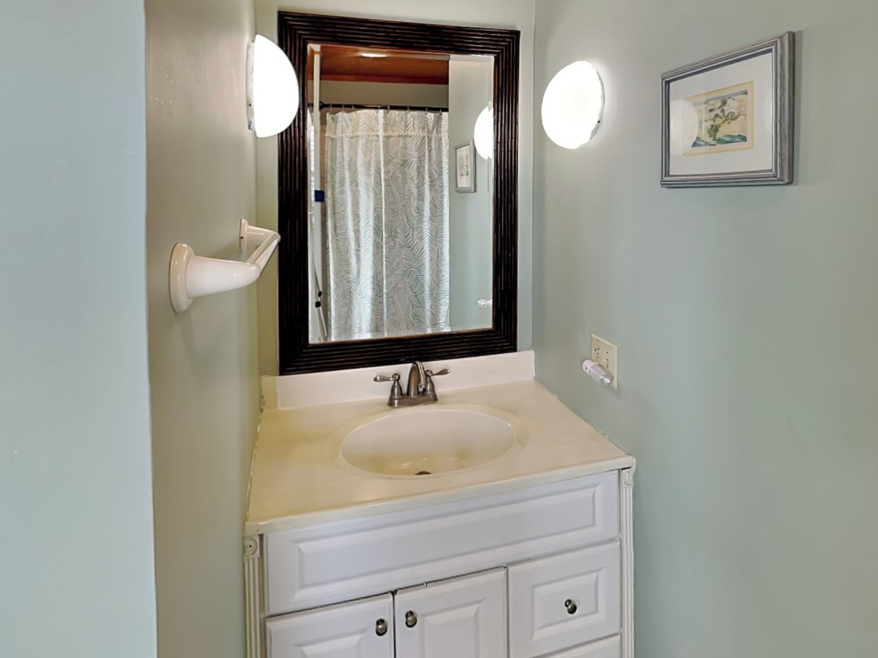 A bathroom with a white sink, a mirror with a wooden frame, and a wall-mounted light fixture.